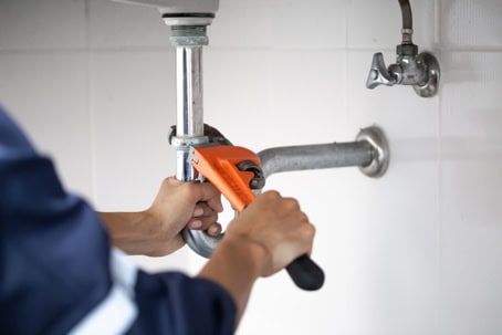 Person Using A Pipe Wrench To Tighten Or Loosen A Pipe Under A Sink.
